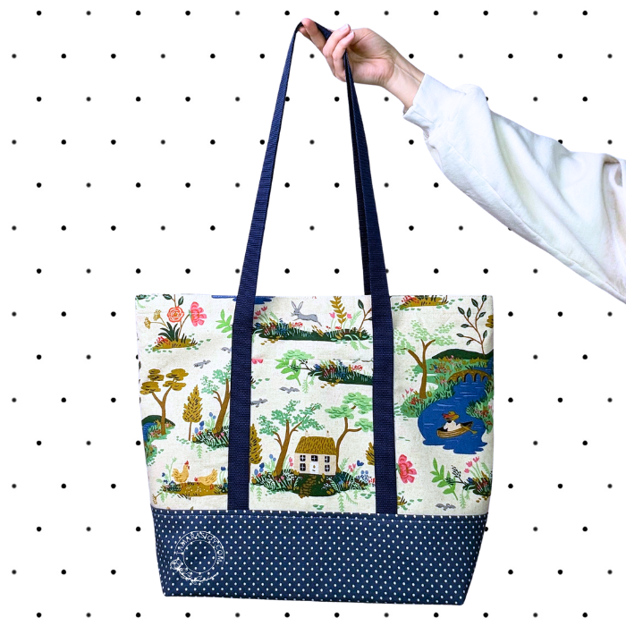 Tote bag with nature-themed design held by a hand against a polka dot background