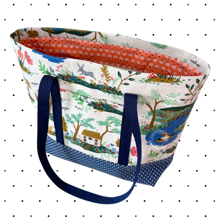 Tote bag with nature-themed design and blue handles on a polka dot background